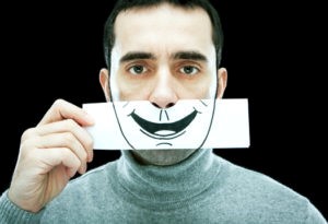 A man showing a blank, indifferent expression, holding the drawing of a smile in front of his face.
